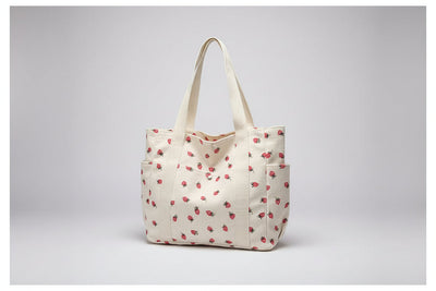 Beige tote bag with red floral pattern on a surface near a window.