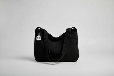 Black corduroy handbag with a keychain on a white surface near a window with blinds.