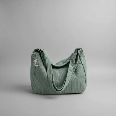 Green corduroy handbag on a white surface with blinds in the background