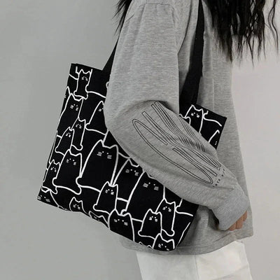 Person holding a black tote bag with white cat patterns against a gray background