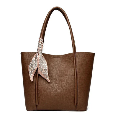 Brown leather tote bag with a decorative scarf on a white background