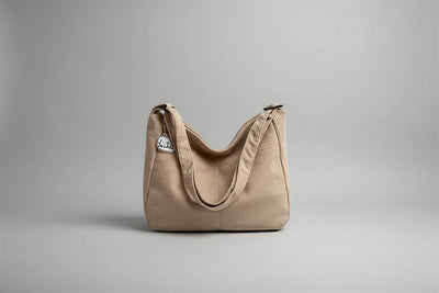 Beige corduroy handbag with a small white cat plushie on a surface with blinds in the background